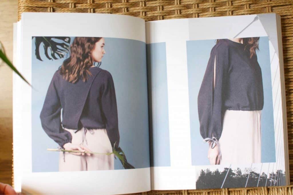Open book displaying sewing patterns. The left page shows a woman in a black top and beige skirt, holding a plant behind her back—perfect inspiration for your Spring Sewing Plans. The right page has a close-up of the tops design, featuring long sleeves with ribbon details. Background is blue.