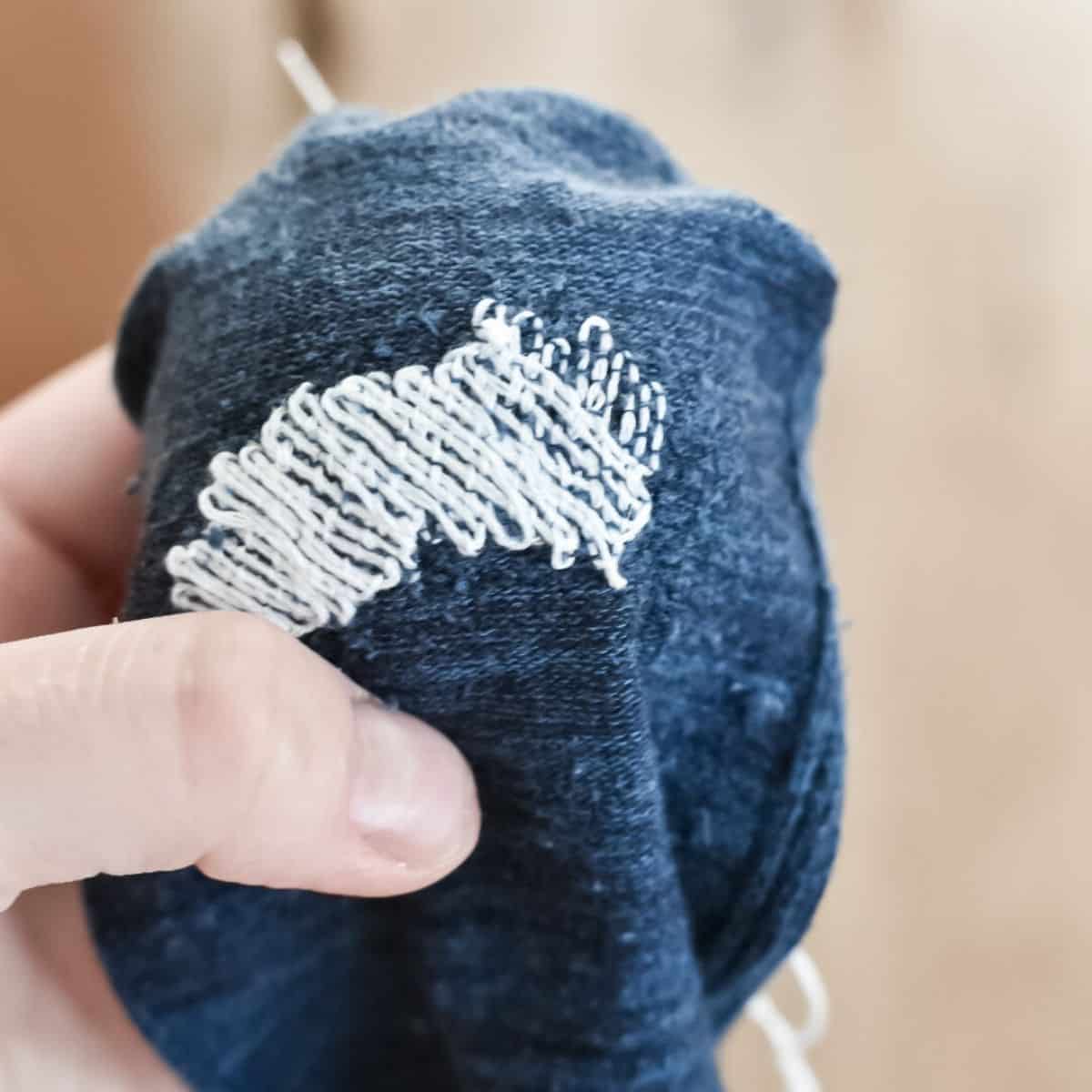 A blue sock that has been darned with white thread