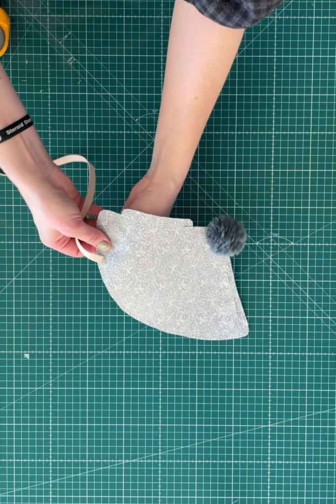 Person holding the DIY party hat over a green cutting mat. She is pushing elastic through one of the holes. Scissors are partially visible in the corner.