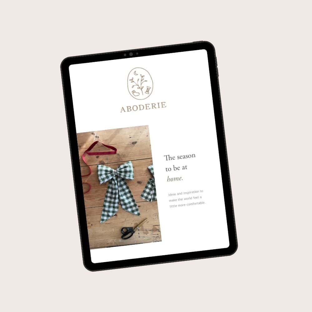A tablet showing the Aboderie newsletter for December. It has a picture of a green gingham bow sewing project and the words 'Tis the season to be at home'