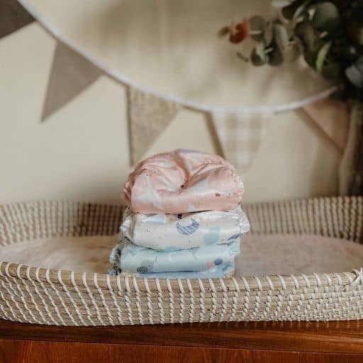 A pile of cloth nappies sits on a basket changing mat with bunting in the background.