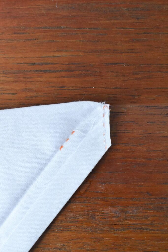 Close-up of a corner of a beautiful handkerchief with orange stitching, resting gracefully on a wooden surface.