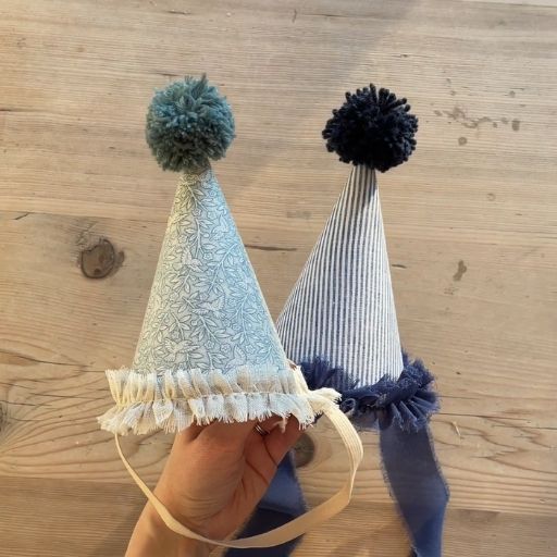 Two blue handmade fabric party hats with wool pom poms and ribbon trim