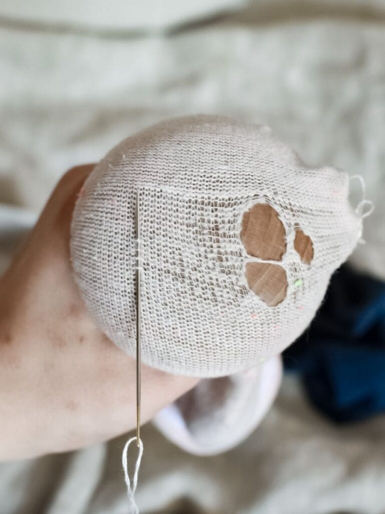 A hand holding a sock stretched over a darning mushroom, with a needle inserted into the fabric, starting the darning process.