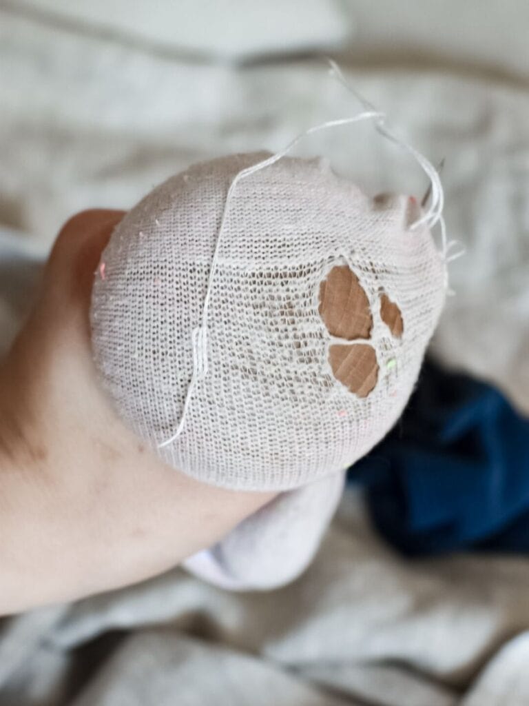 A sock with a large hole, stretched over a darning mushroom, as white thread begins to form the first stitches of the repair.