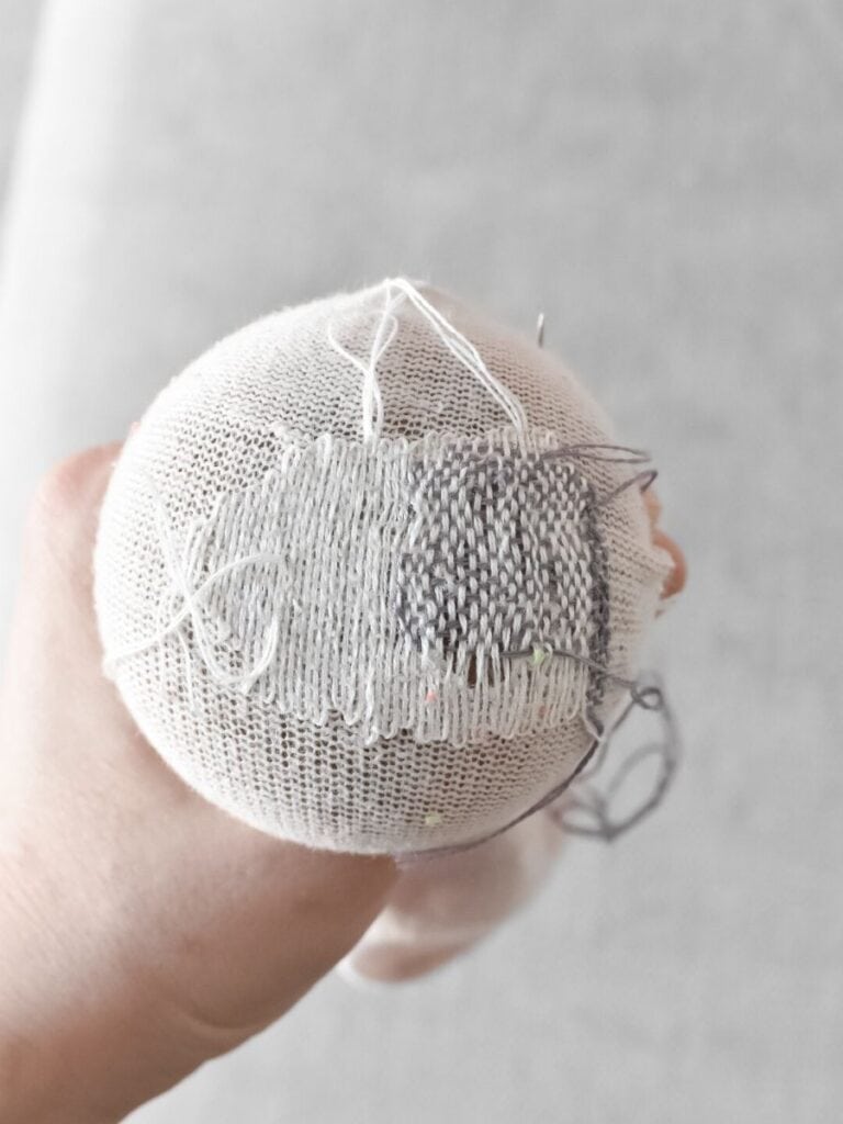 A completed darn on a sock, showing a woven pattern of grey and white stitches creating a sturdy mend.