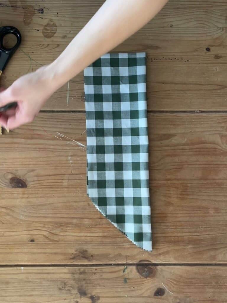 A piece of green and white gingham fabric with one end cut into a diagonal point, forming the tails of the fabric bow.