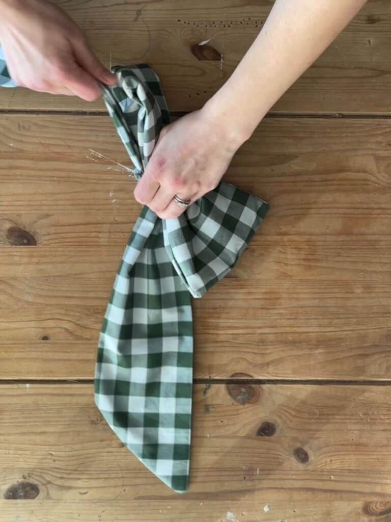 Hands gathering the center of the fabric bow, adjusting the folds to create a full, structured shape before securing the middle knot.