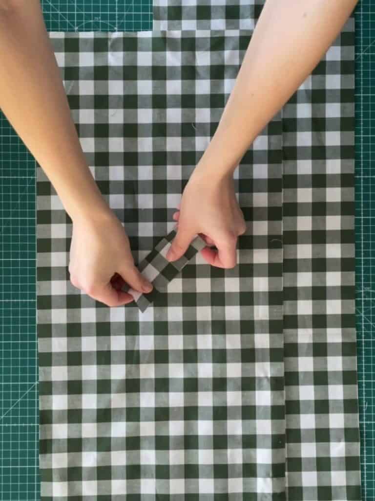 Hands folding and aligning the fabric pieces on a cutting mat, ensuring accurate placement for a well-proportioned bow.