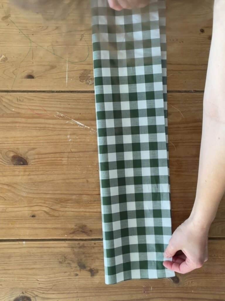 The gingham fabric neatly folded on a wooden table, showing the initial steps of shaping the bow structure.