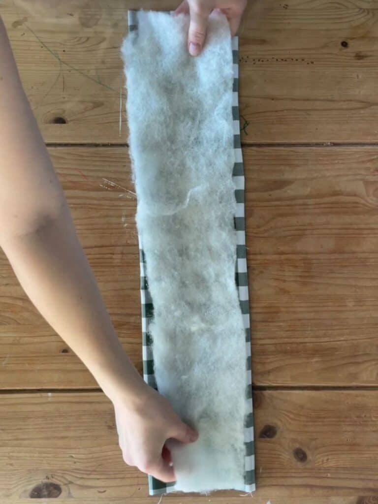 A layer of soft wadding is placed inside the fabric strip to add volume to the bow, giving it a structured and plush appearance.