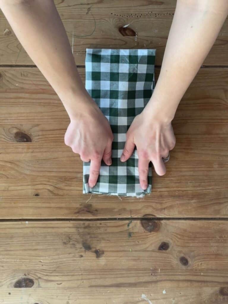 Hands pressing the folded gingham fabric, ensuring neat creases for assembling the bow’s loops and tails.