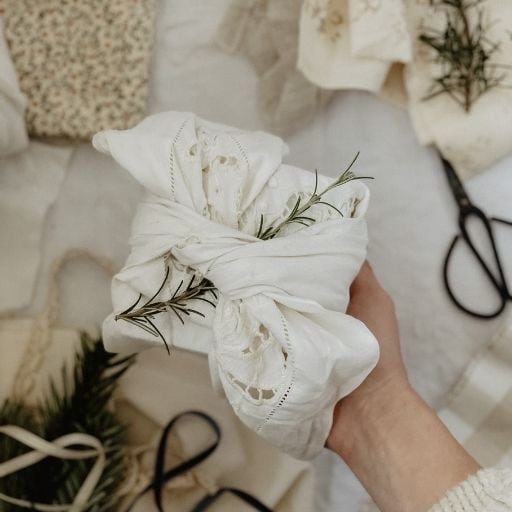 A gift wrapped with the furoshiki method using a vintage napkin. There is a sprig of rosemary to decorate.