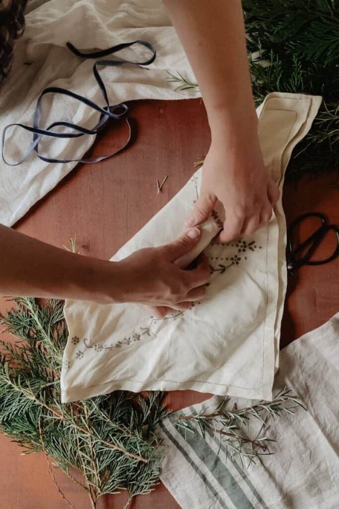 A gift being wrapped using the furoshiki method, using a vintage linen. One corner of the linen has been tucked under the gift