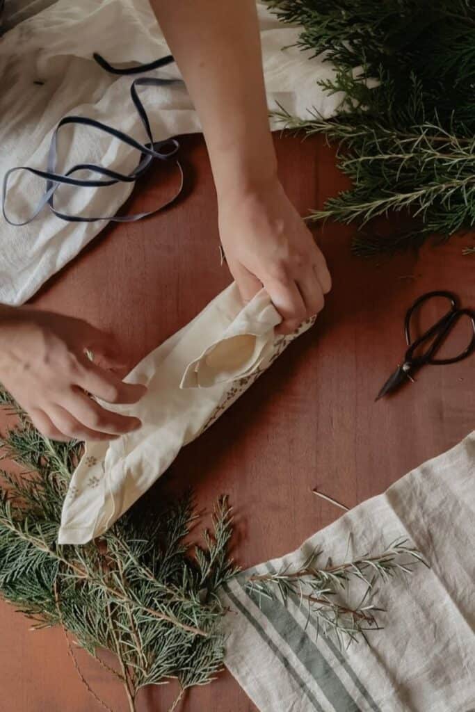 A gift being wrapped using the furoshiki method, using a vintage linen. One of the remaining corners has been pinched together and brought over the top of the gift.