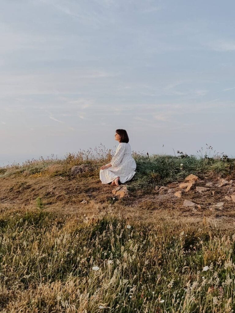 Innes sits on a grassy bank with a blue sky in the background