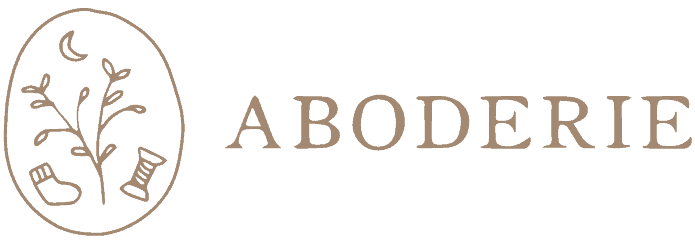 Logo for ABODERIE featuring a stylized tree within a circular border, accompanied by a sock and a comb. The color scheme is a simple brown on a transparent background.