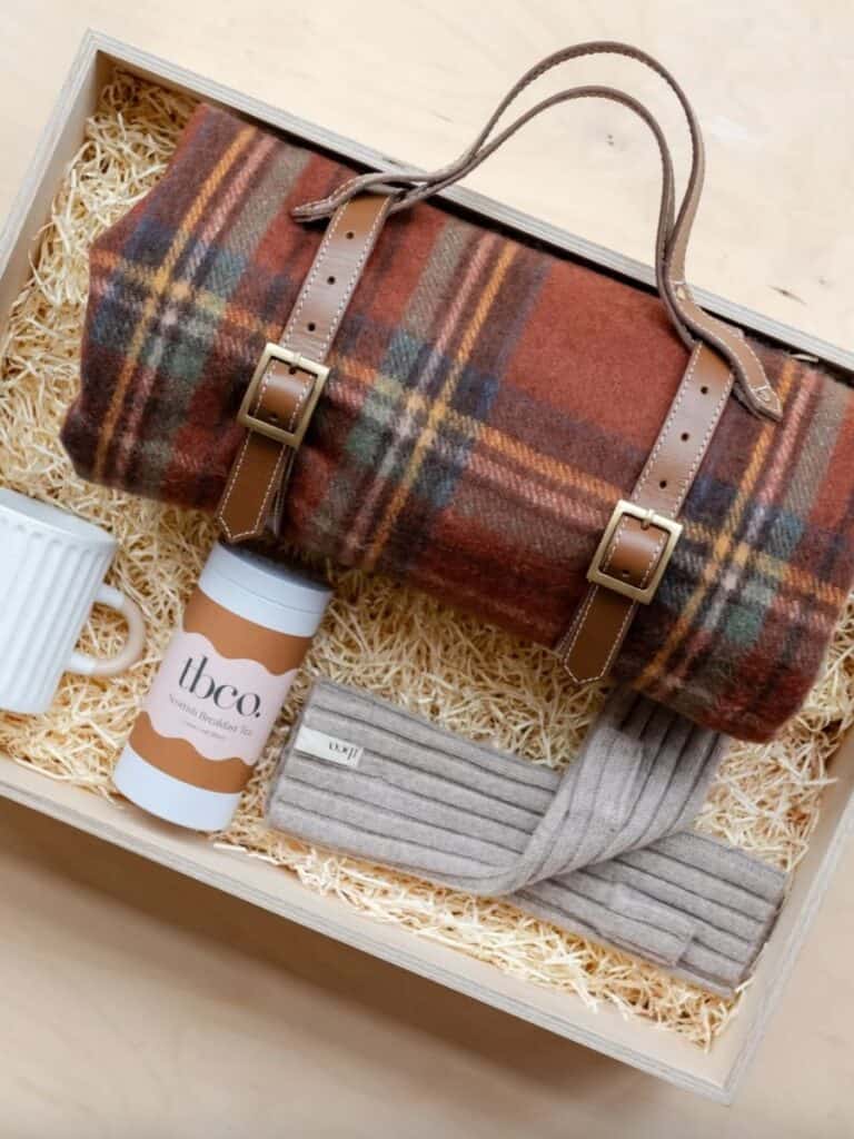 A cozy gift box featuring a rich brown wool TBCo blanket, loose-leaf Scottish breakfast tea, a ribbed headband, and a ceramic mug—a warm and thoughtful present.