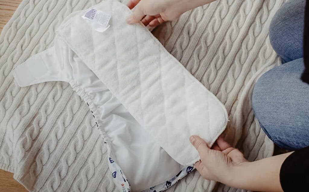 Hands carefully hold the inner cloth liner of a Bambino Mio cloth nappy on a woolen blanket, showcasing the the absorbency of the reusable nappy.
