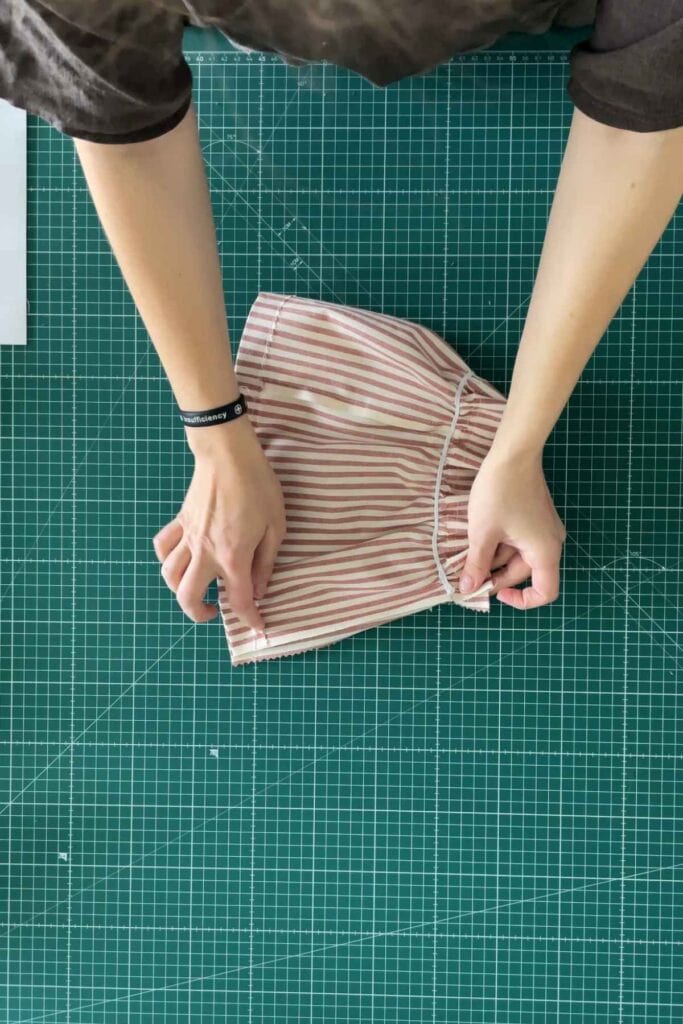 Person folding a red and white striped DIY gathered lampshade on a green cutting mat. 