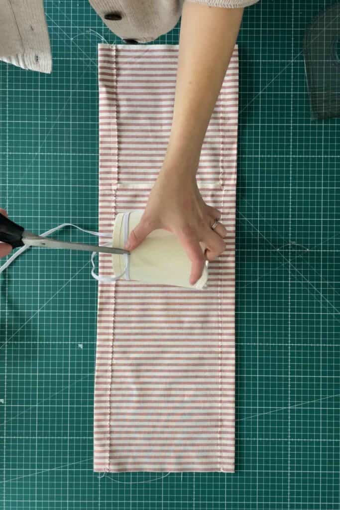 A person measures a piece of elastic around a lampshade, on top of a piece of red and white striped fabric.