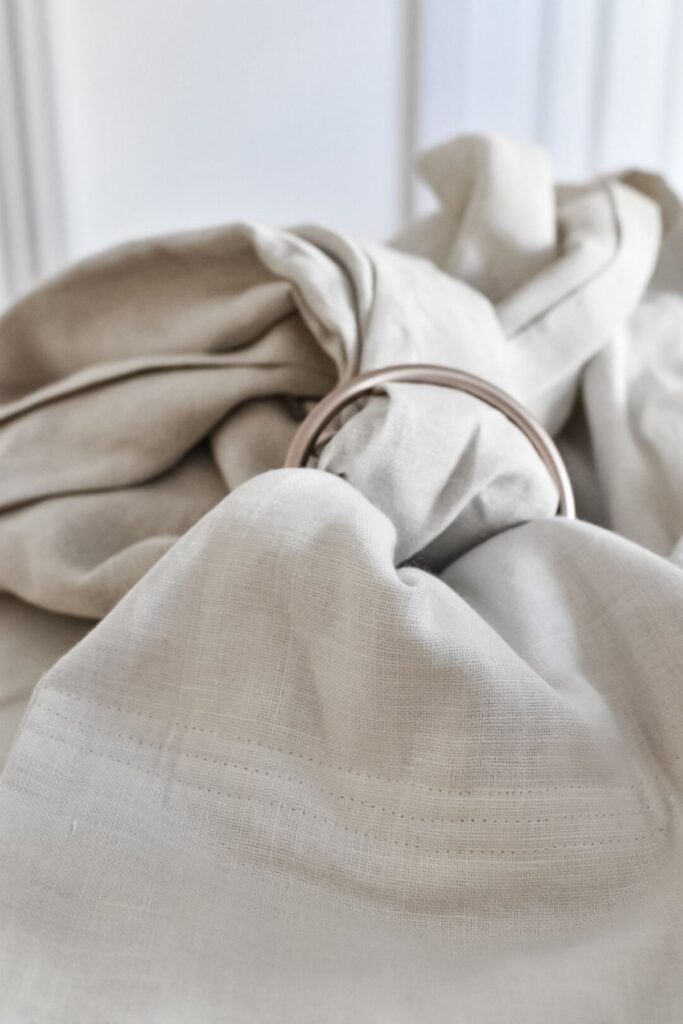 Close-up of light beige, DIY linen ring sling gathered with an antique gold sling ring. The subtle weave texture and gentle folds evoke elegance, making it perfect for a nurturing baby carrier.