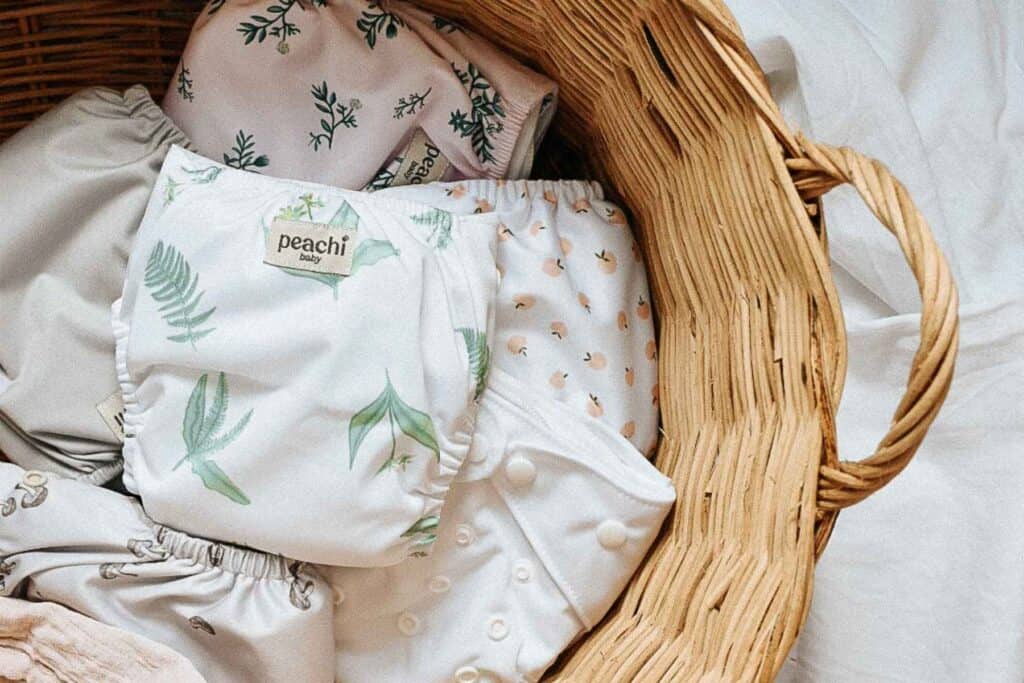 A wicker basket brimming with baby cloth nappies by Peachi baby showcases delightful patterns of leaves and small animals. Perfect for eco-friendly parenting, these designs support sustainable family practices.