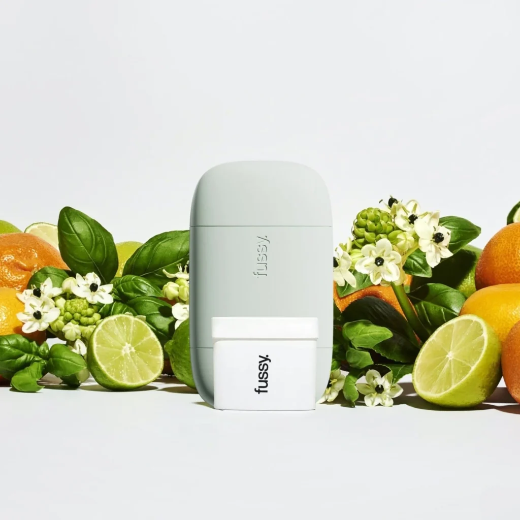 A fussy deodorant refill case and refill against a backdrop of citrus fruits and flowers