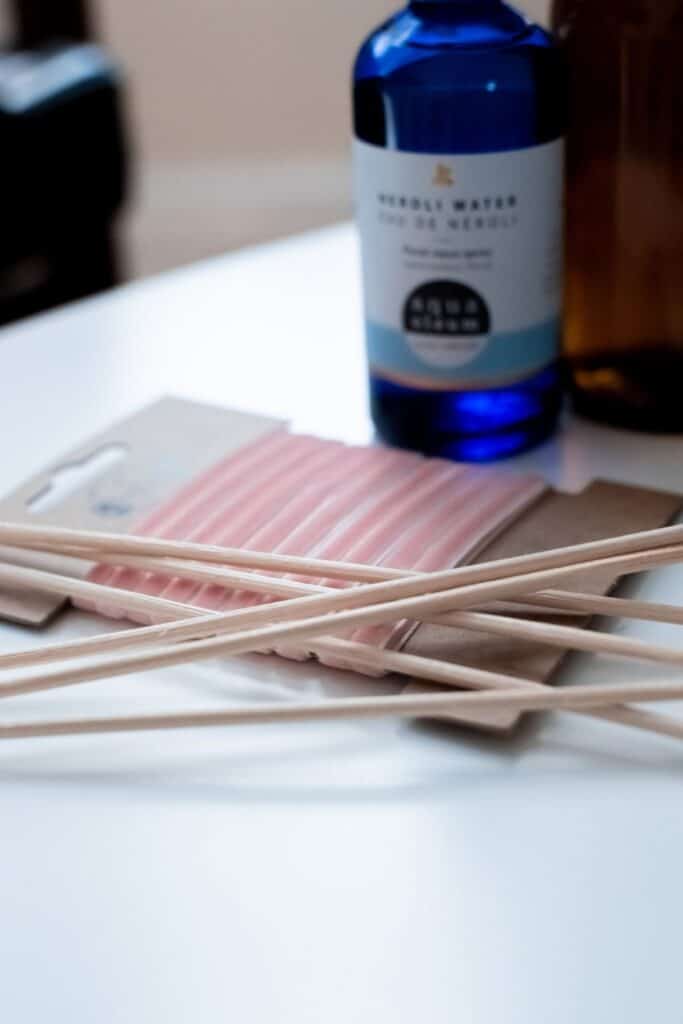 A bundle of light pink incense sticks rests on a table, their wooden stems casually scattered. Nearby, a blue bottle of herbal water peeks into view. Ideal for crafting handmade wedding gifts, this aromatic set brings tranquility and charm to any DIY project.