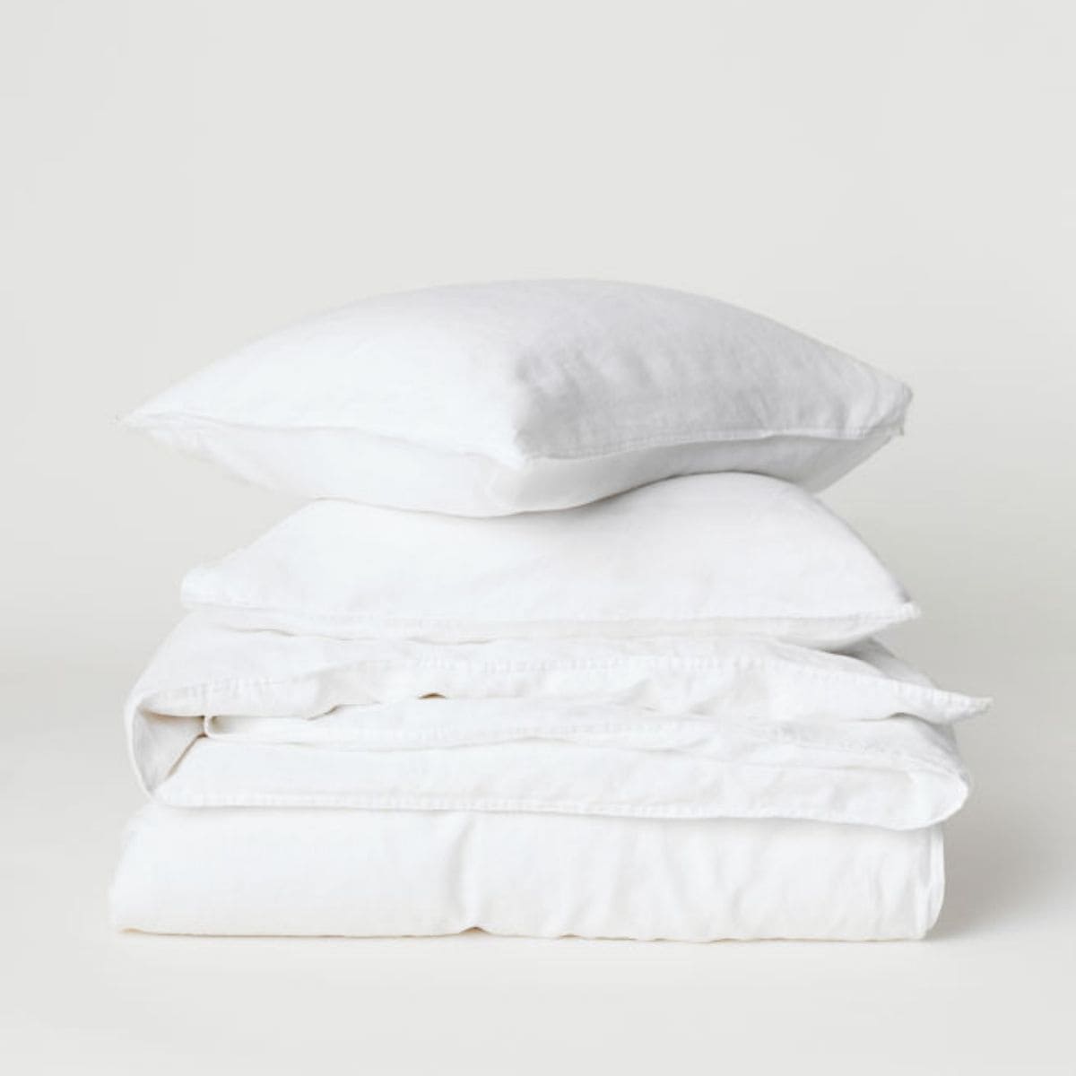 A neatly folded stack of fresh white linens, including two pillows and sheets, against a plain background.
