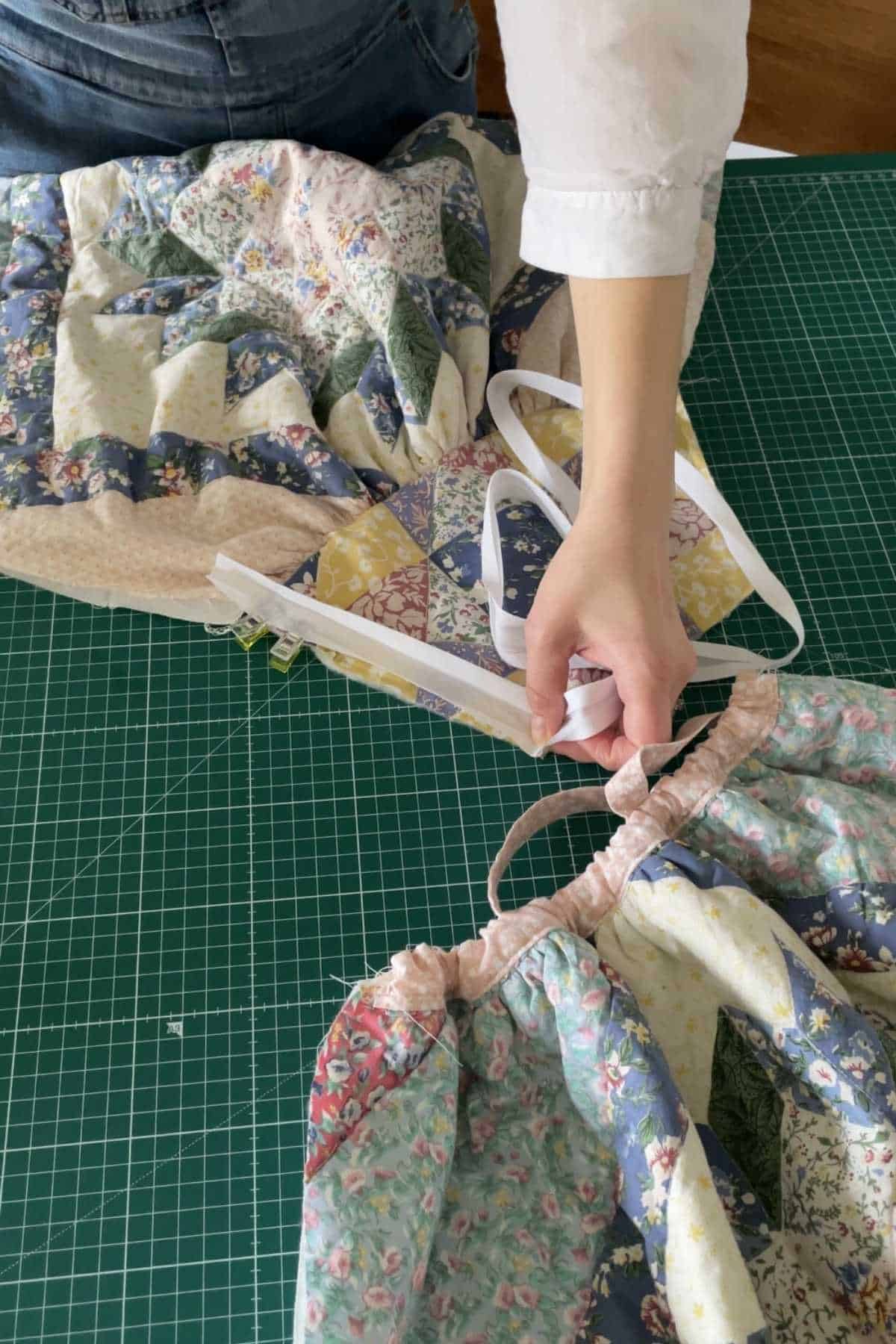 Person sewing a colorful quilt on a green cutting mat. Holding a measuring tape, they work with floral and patterned fabric pieces. The old quilt features various triangular patches in multiple colors and patterns, reminiscent of creating a beautiful patchwork dress.