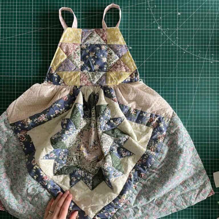 A handmade patchwork dress with floral patterns in blue, green, and yellow, is laid out on a green cutting mat.
