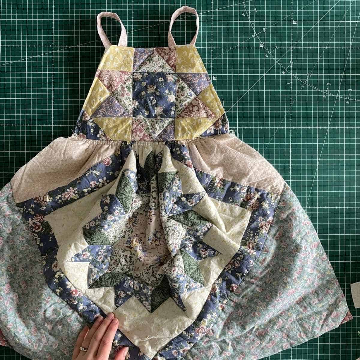 A handmade patchwork dress with floral patterns in blue, green, and yellow, is laid out on a green cutting mat.