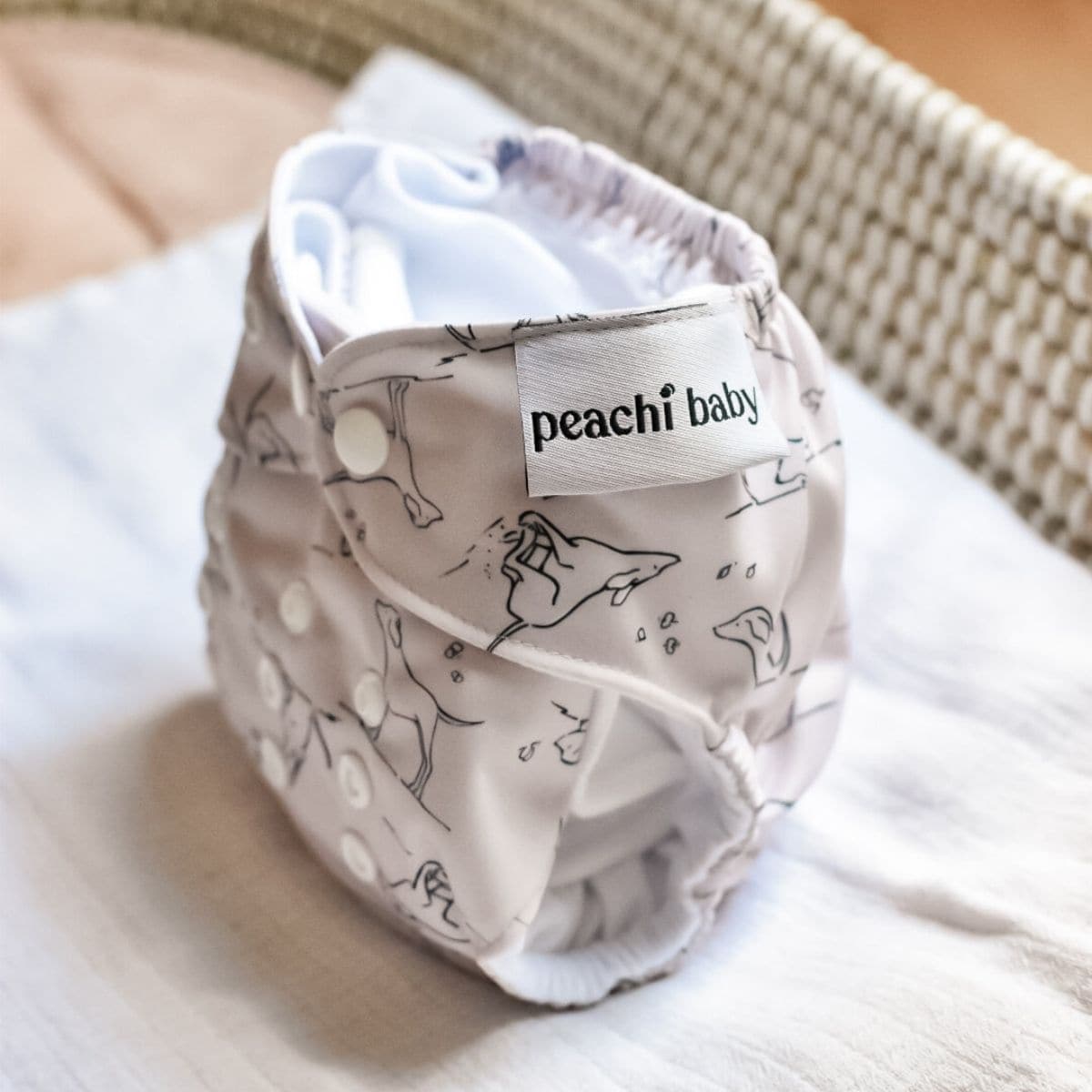 A charming cloth nappy featuring delightful animal patterns and the signature Peachi Baby label, beautifully displayed on a white cloth.