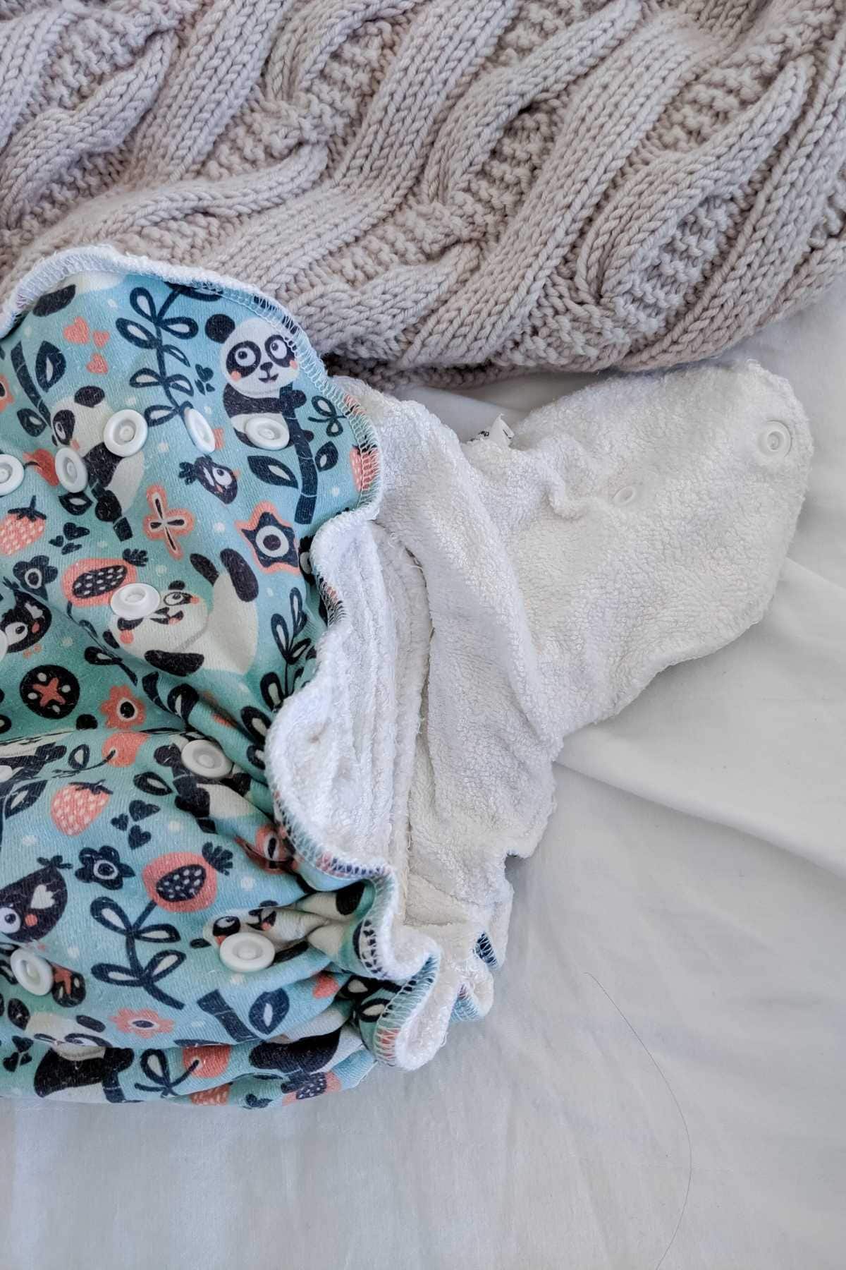 A patterned Petit Lulu cloth nappy with pandas and leaves sits on a white surface. 