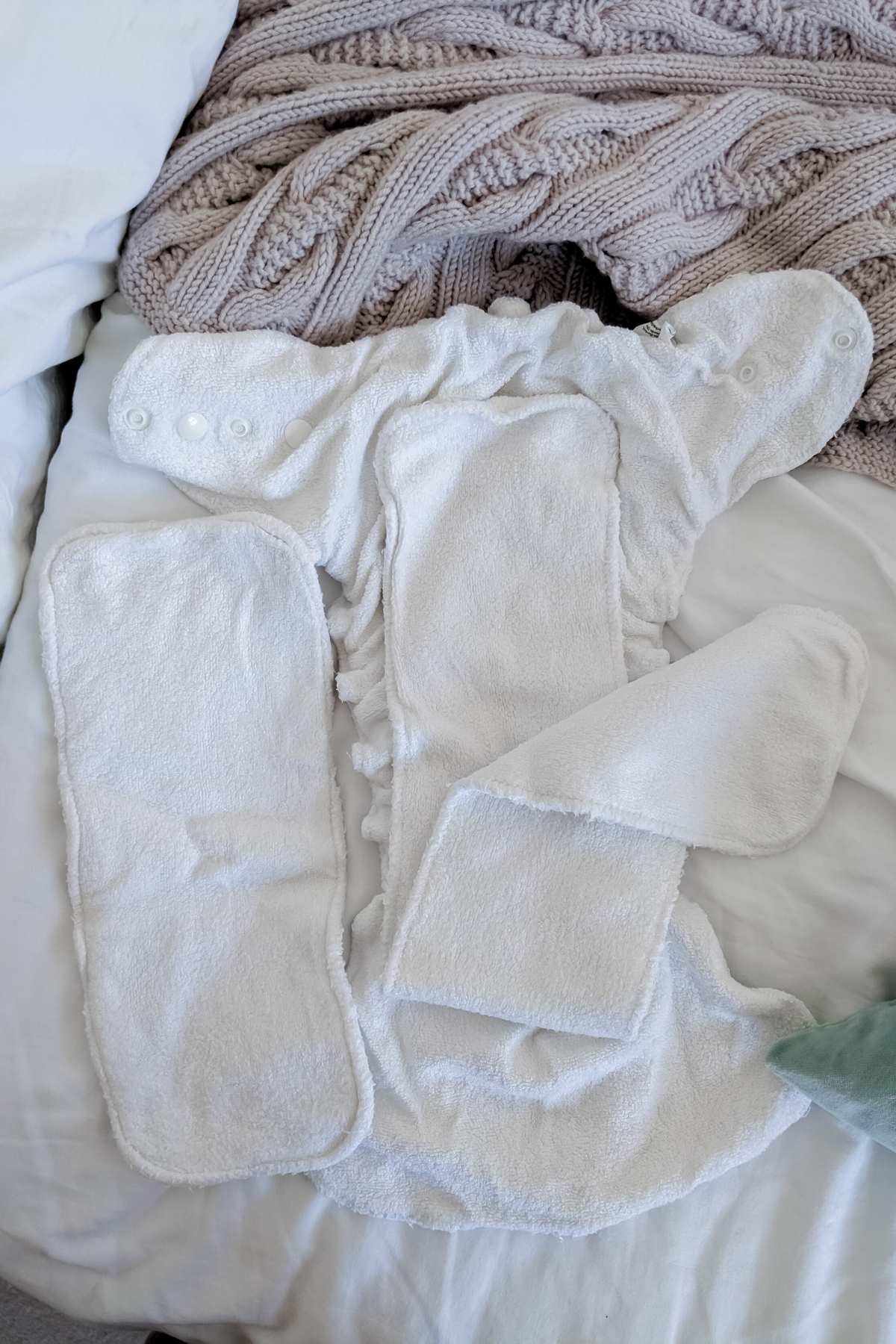 A Petit Lulu fitted cloth nappy is laid open on a bed, with a knitted beige blanket in the background. Extra inserts accompany this fitted nappy option, showcasing its design and functionality for those seeking a reliable choice.