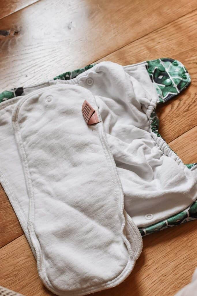 A Petite Crown Trima Nappy, with its vibrant outer fabric and soft white inner lining, is laid open on a wooden floor.