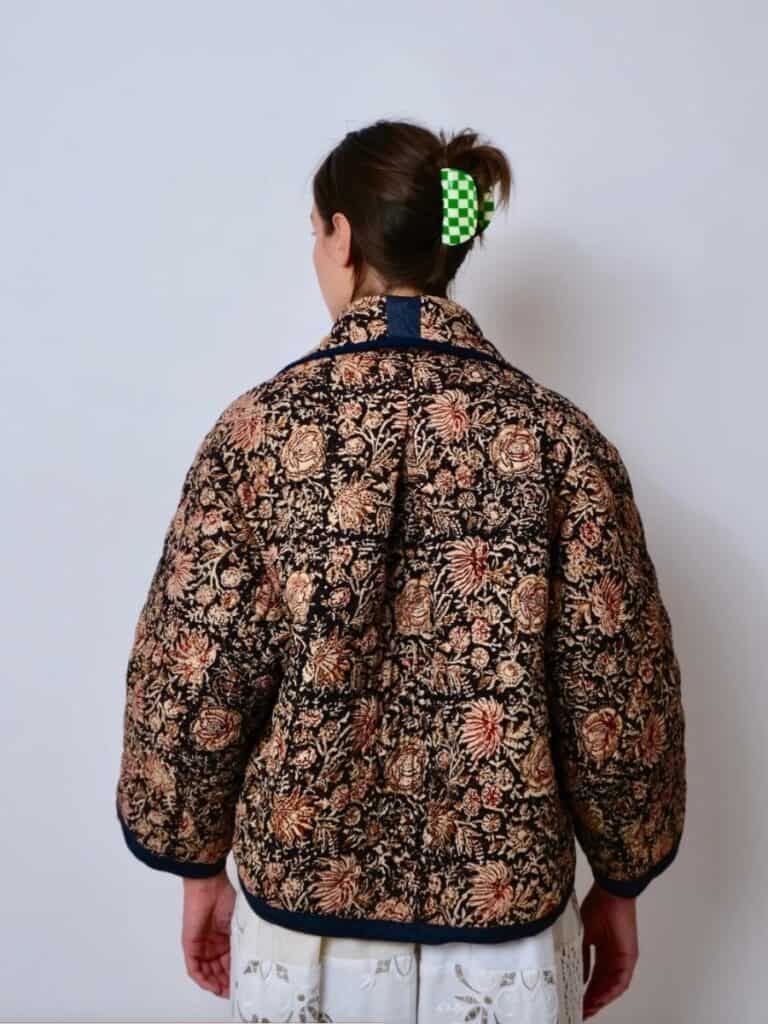 A back view of a quilted Birgitta Helmersson floral jacket with warm autumnal tones, worn over a lacy white skirt. The jacket is reminiscent of a handmade, upcycled quilt, perfect for layering in a cottagecore wardrobe.