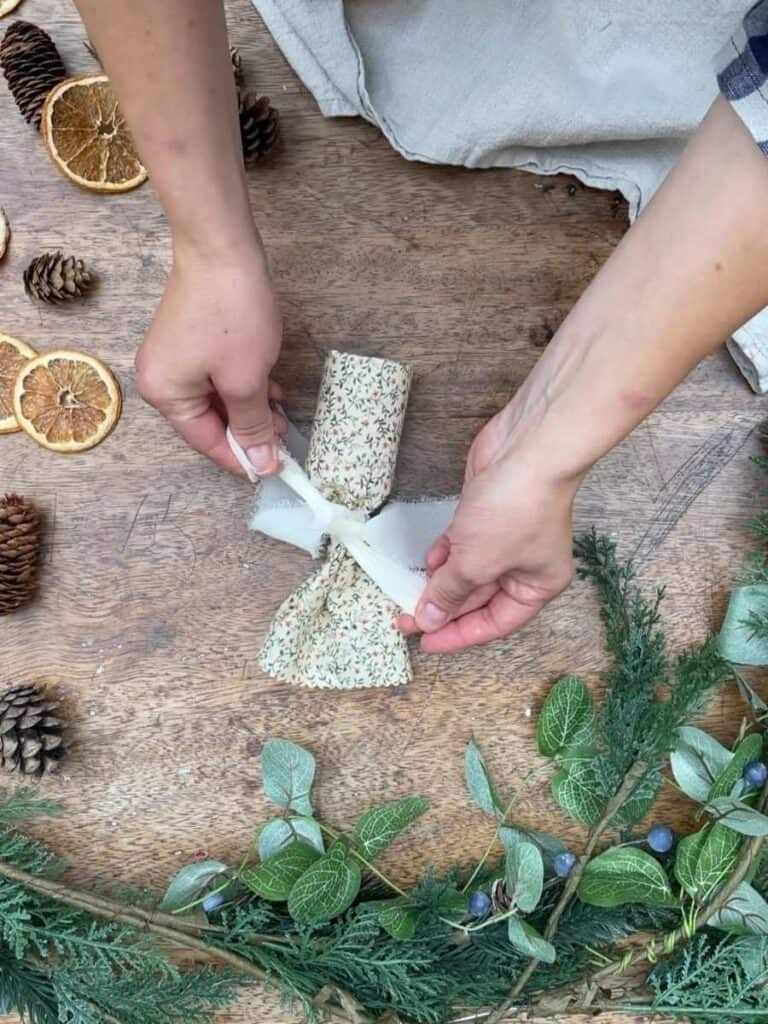 A person tying white ribbon around one end of a reusable Christmas cracker.