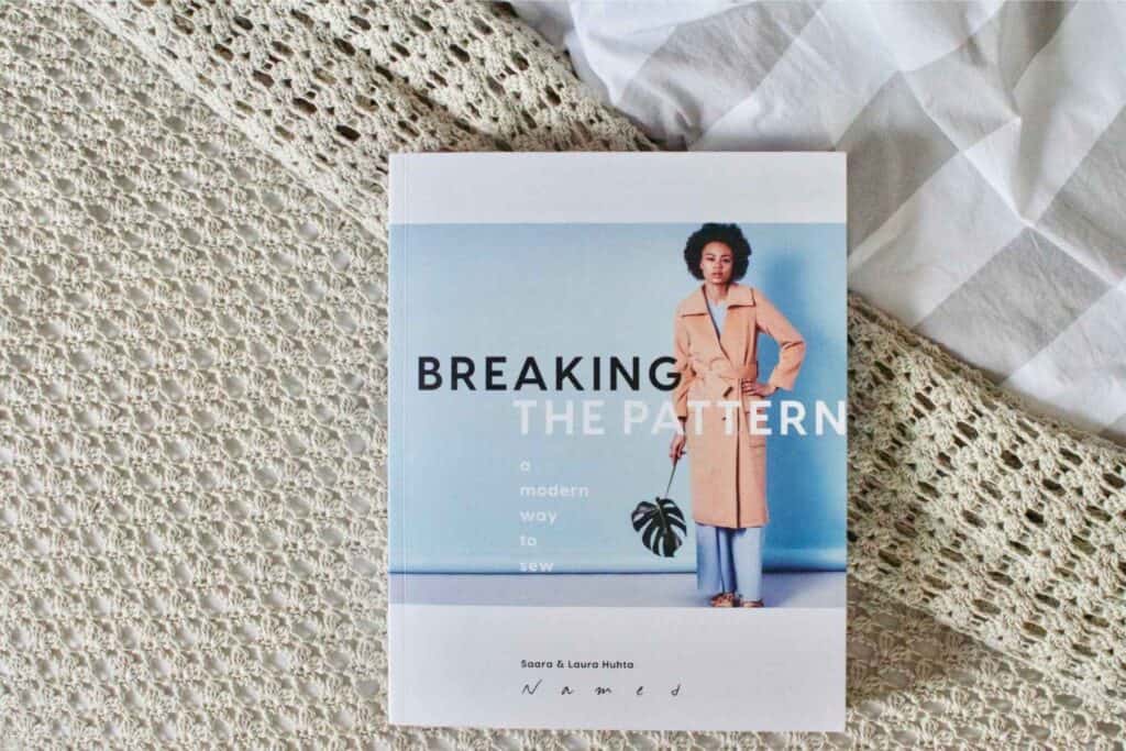 A book titled Breaking the Pattern rests on a textured surface, perfect for those planning their spring sewing projects. The cover features a person in a long coat holding a large leaf against a blue background. The authors, Saara & Laura Huhta, offer inspiring ideas for your sewing plans.