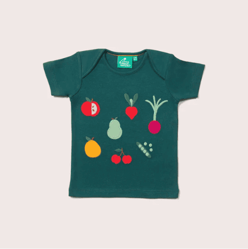 A green childrens Little Green Radicals t-shirt featuring colorful illustrations of various fruits and vegetables, including a tomato, radish, carrot, pear, orange, peas, and cherries, arranged across the front.