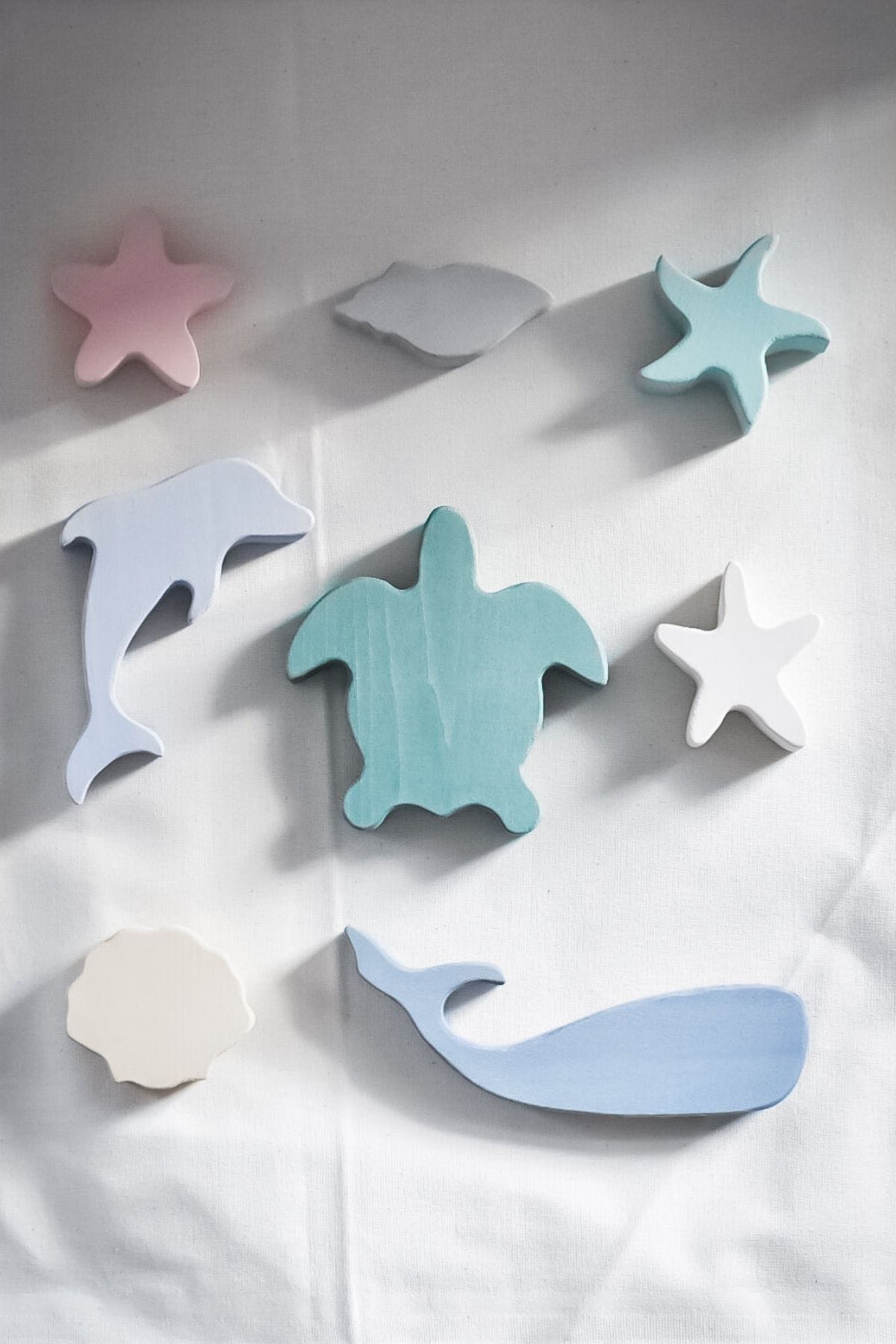 Pastel-colored wooden toys from sustainable toy brand Raduga Grez, including a dolphin, turtle, and abstract shapes in shades of blue, pink, and cream, adorn a light surface. 