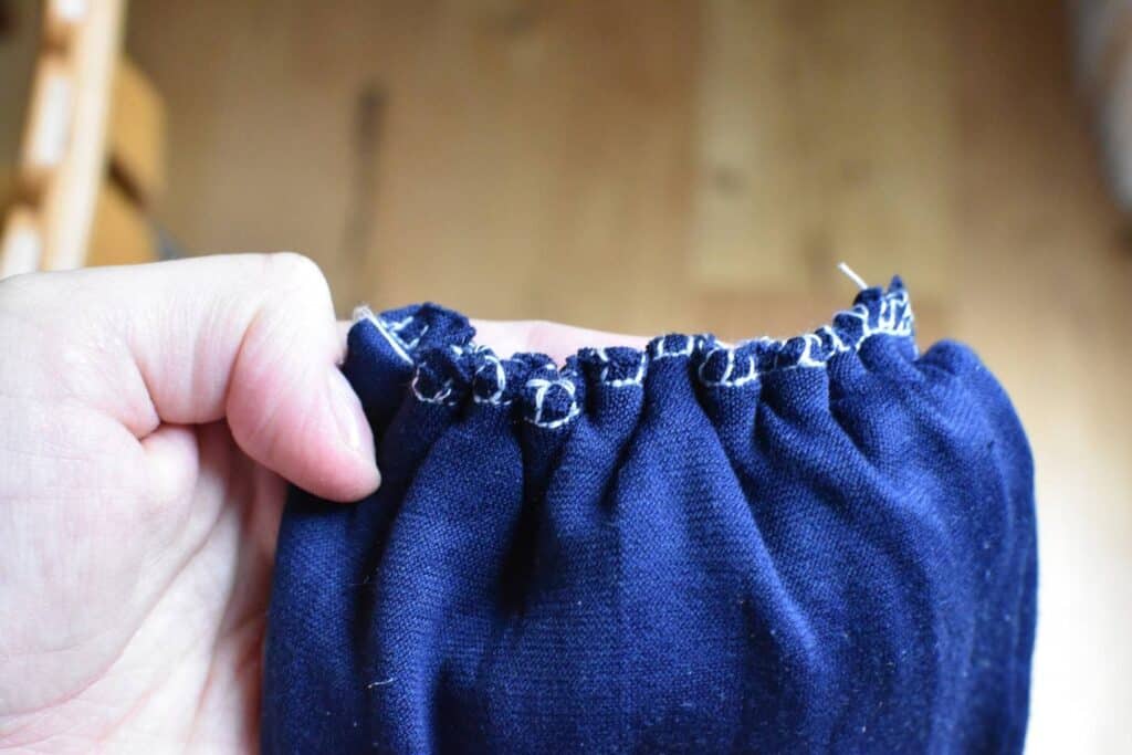 A hand is holding the baby turban hat with gathered stitches along the top edge. 