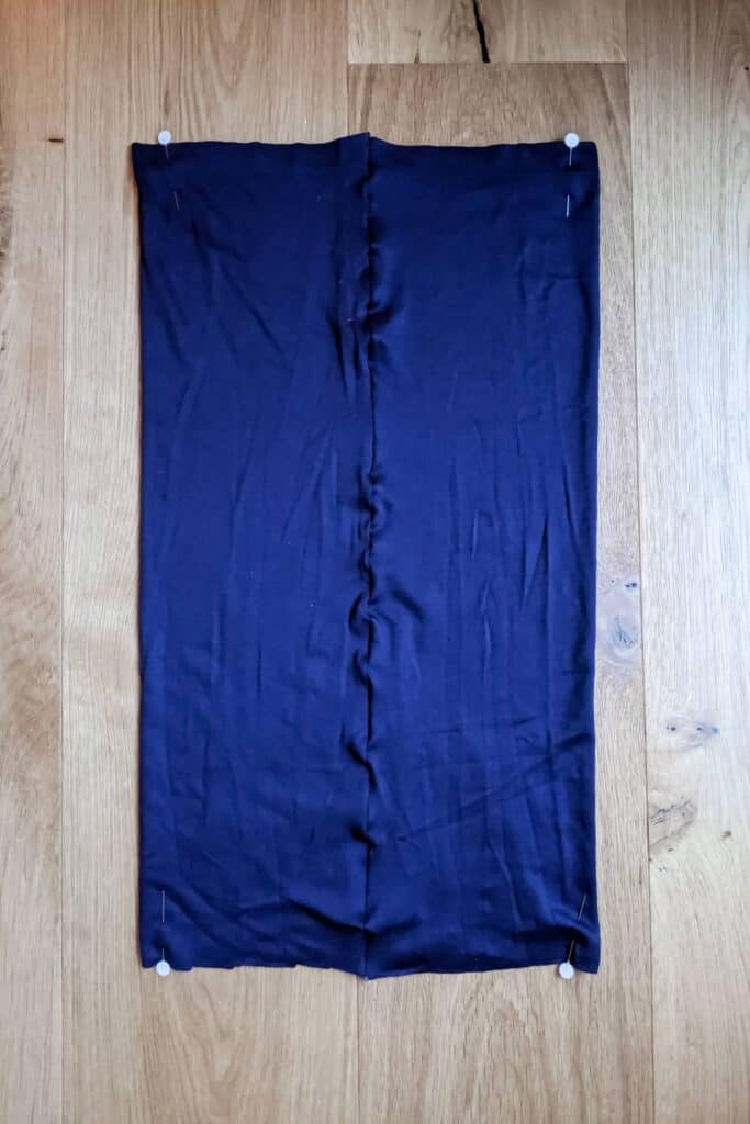 A dark blue fabric tube, once part of an old dress, is pinned at the corners. Rectangular in shape, it has slight wrinkles along the center where the seam is.
