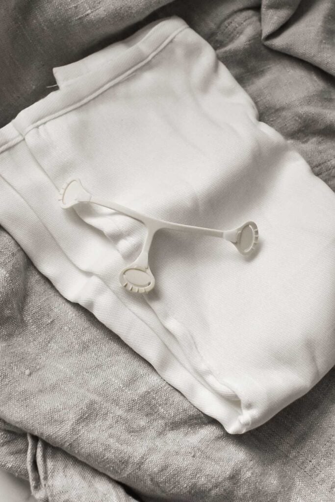 A white eyelash curler rests on folded white and gray fabric, reminiscent of the soft textures found in a cloth nappy. The neutral shades of white and gray create a serene atmosphere, perfect for any guide on beauty essentials.