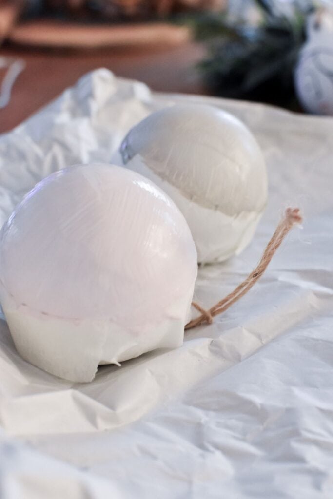 Two white ceramic baubles in the process of being painted with acrylic paint.