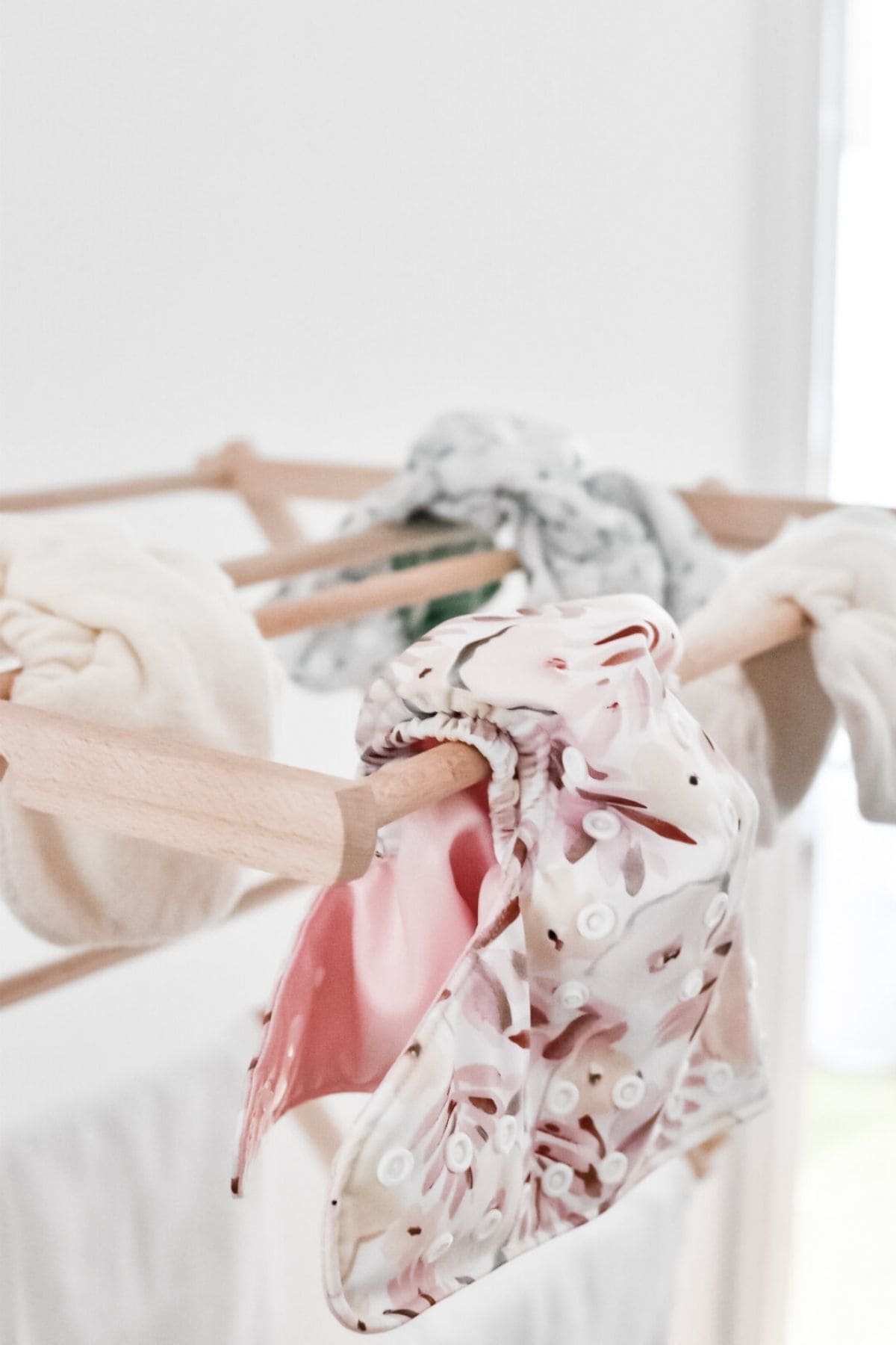 Freshly washed cloth nappies with vibrant prints hang on a wooden drying rack indoors.