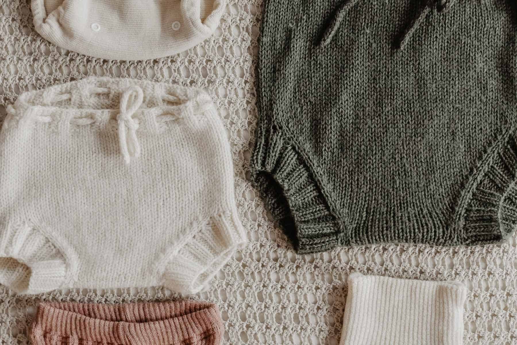 A selection of wool nappy covers on a textured surface in white and olive green, all perfectly arranged in a charming flat lay.